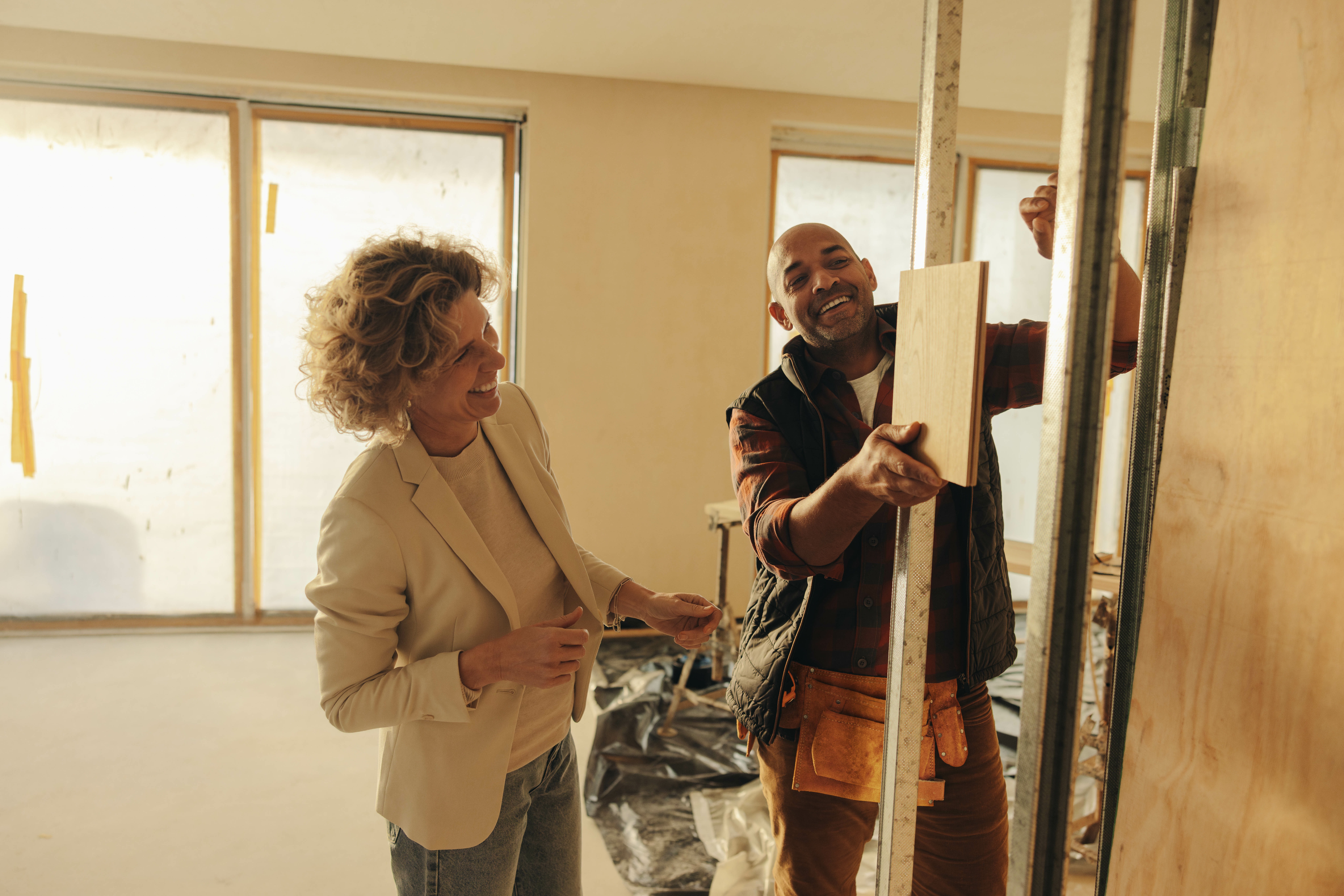 Happy contractor and interior designer plan a renovation inside a house. They discuss the doors, matching a wood sample against a doorframe for the interior remodel. Collaboration for a property upgrade.